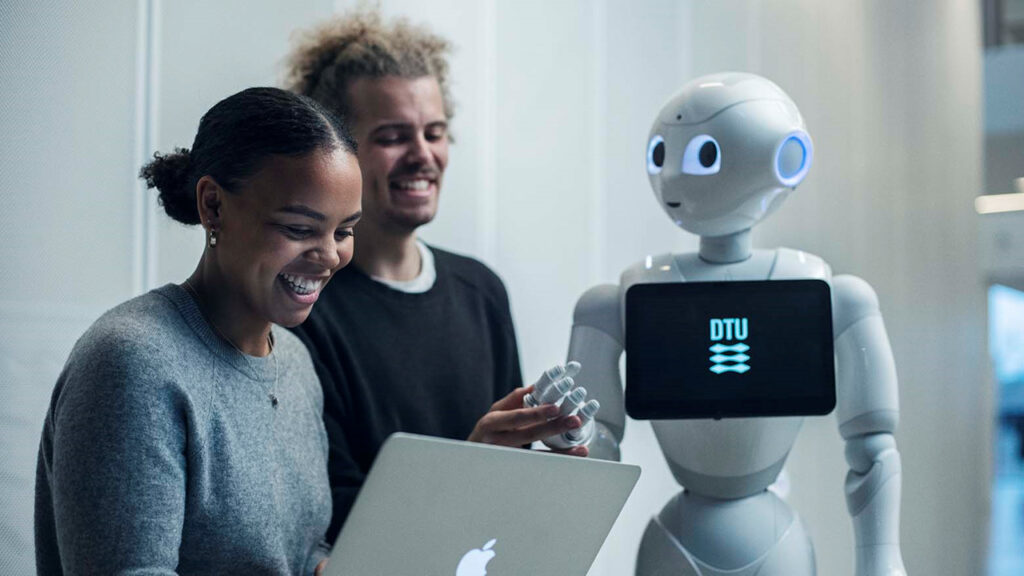 A female and a male student of Technical University of Denmark, talking to a 120-centimetre tall humanoid robot, which is to carry out teaching and research tasks.