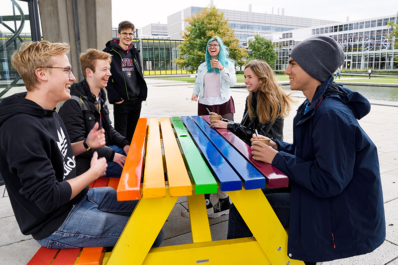 A diverse group of TU/e students gathering round a table in rainbow colours